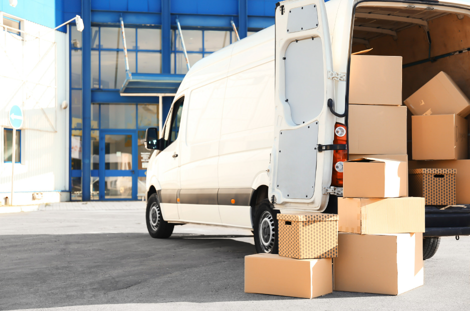 Furgoneta blanca con las puertas traseras abiertas y cajas de cartón apiladas junto a ella